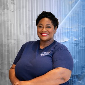 A black woman in a blue short-sleeve shirt smiles.