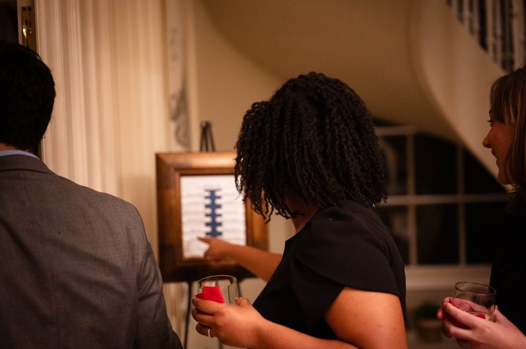 A woman pointing to a where she is on a seating chart for dinner while holding a drink