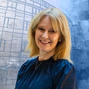 A white woman with blonde hair in a blue shirt smiles with a graphical image of a building behind her.