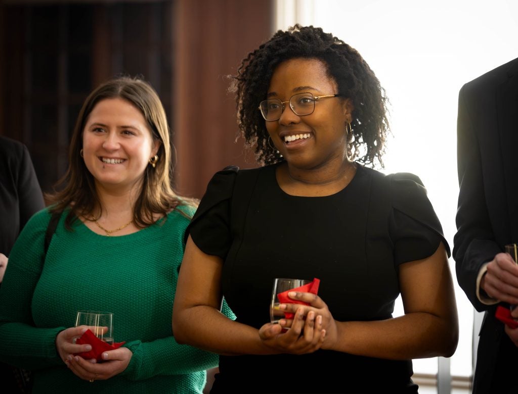 A woman listens and smiles with a drink in hand