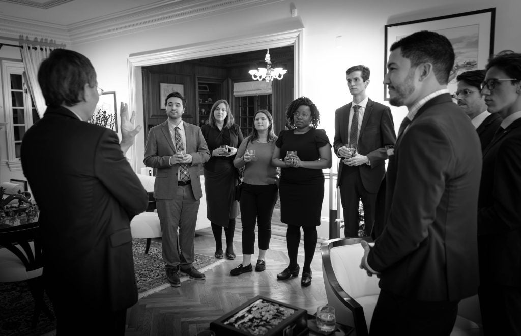 Black and white image of people standing in a circle in a parlor with drinks