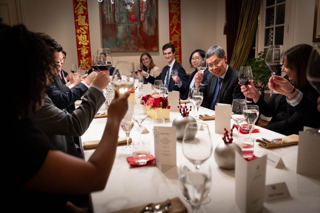 Group of students with an ambassador at a formal dining table raising glasses to toast