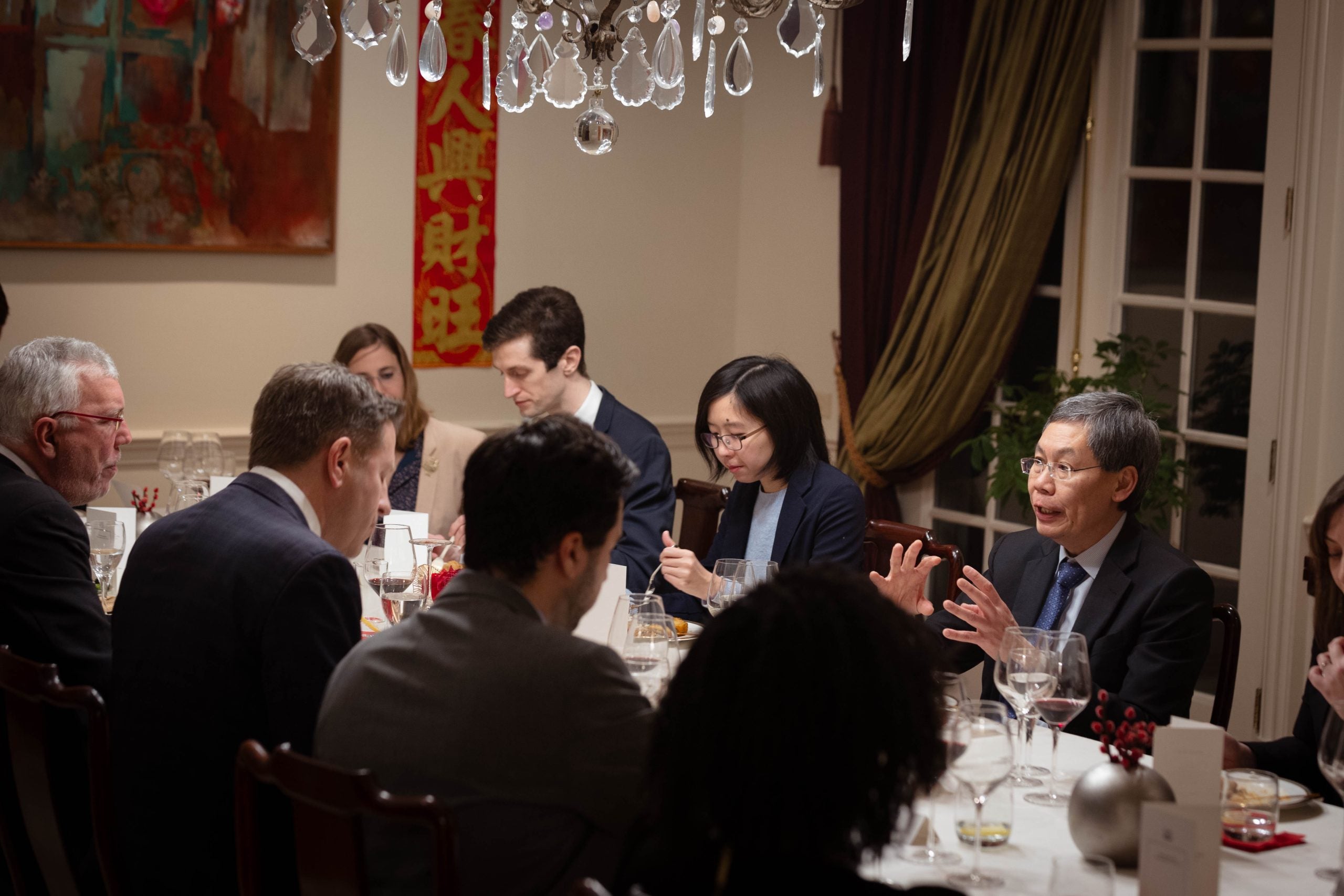 A man talks at a table of people during a formal dinner 