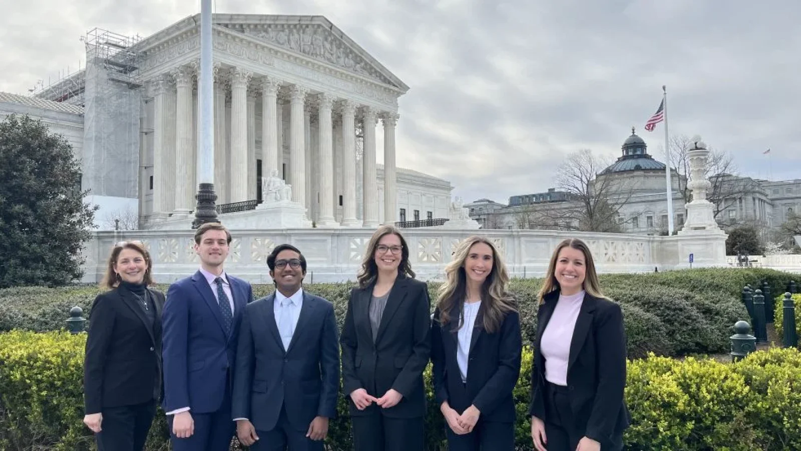 A group of law students stand in front of the columns of the Supreme Court.