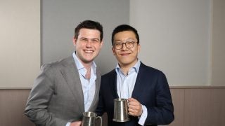 Two male Georgetown students dressed in suits hold metal cups, a prize for a debate tournament.