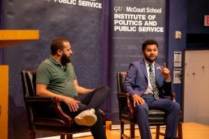 Two men sit on stage discussing politics in front of a crowd of students.