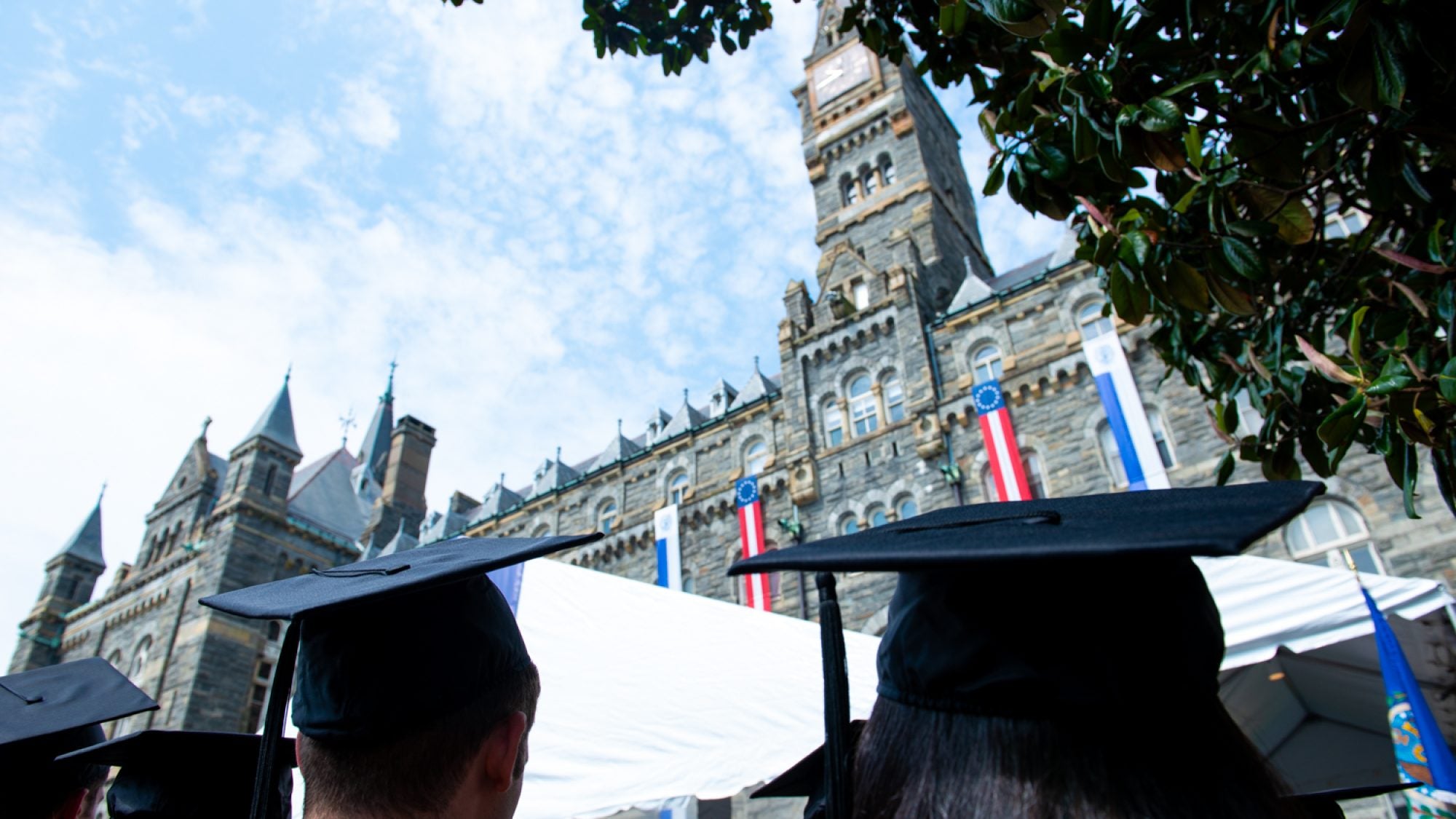 Students in graduation caps look up at the clocktower of Healy Hall.
