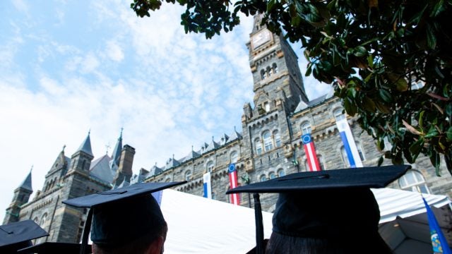 Students in graduation caps look up at the clocktower of Healy Hall.