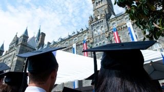 Students in graduation caps look up at the clocktower of Healy Hall.