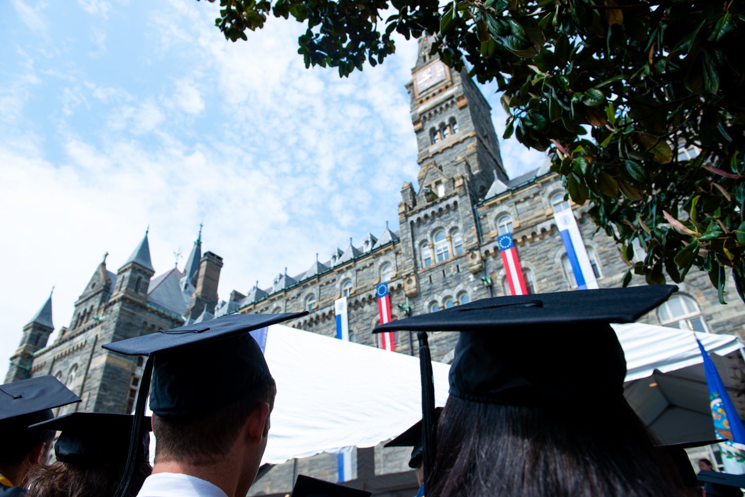 Students in graduation caps look up at the clocktower of Healy Hall.