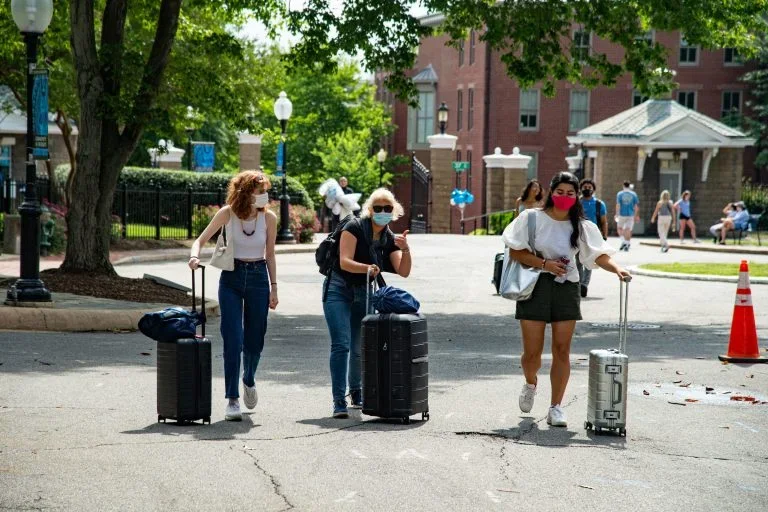 Students in masks rolling up suitcases at Georgetown