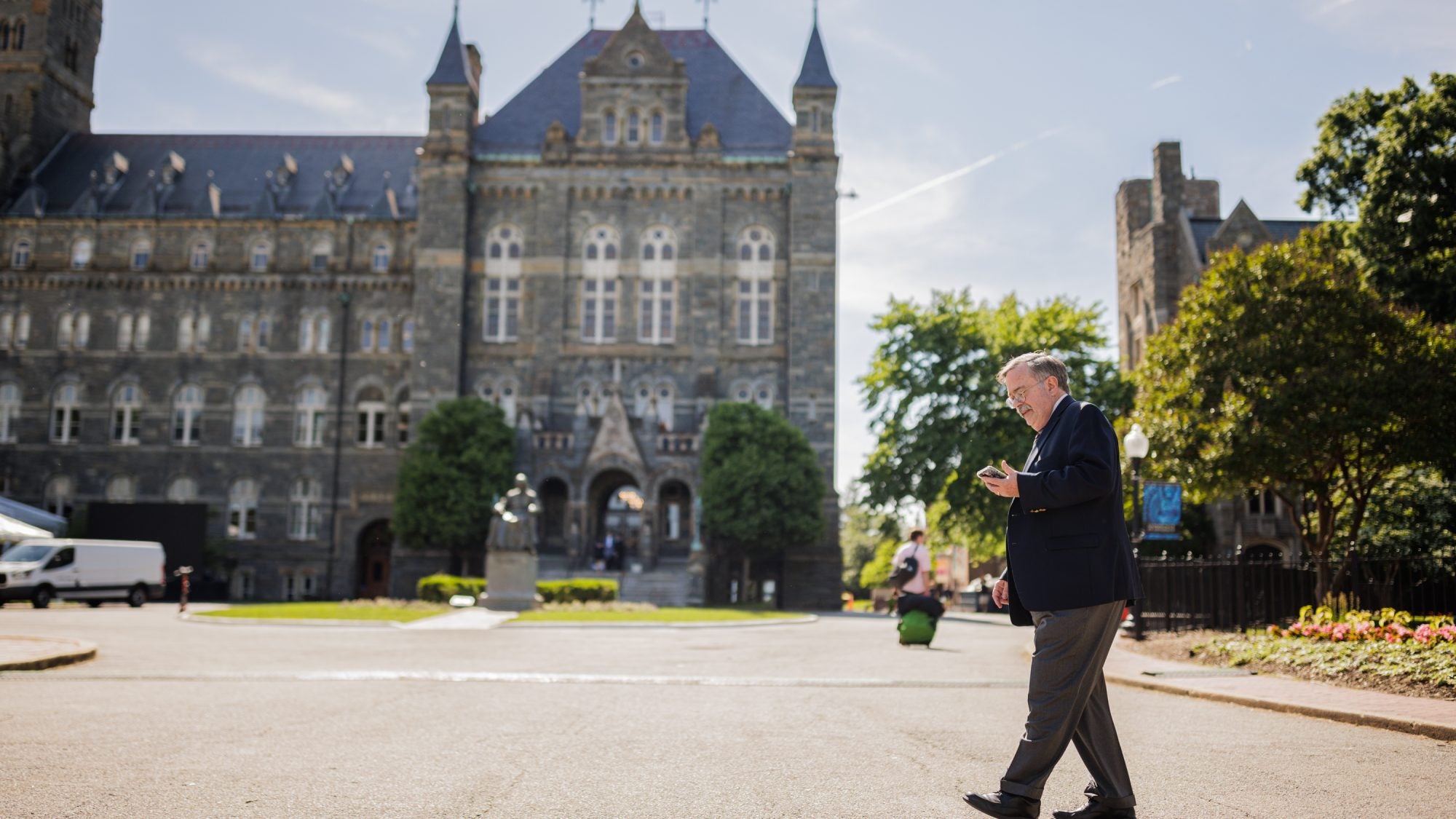 A man with gray hair walks across the entrance to Georgetown and looks at his phone.