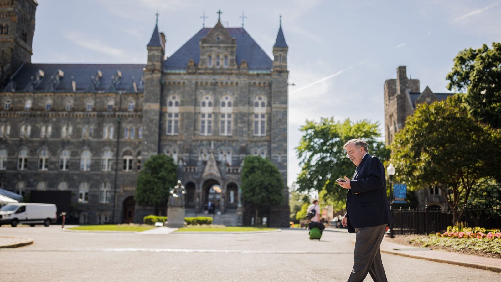 A man with gray hair walks across the entrance to Georgetown and looks at his phone.