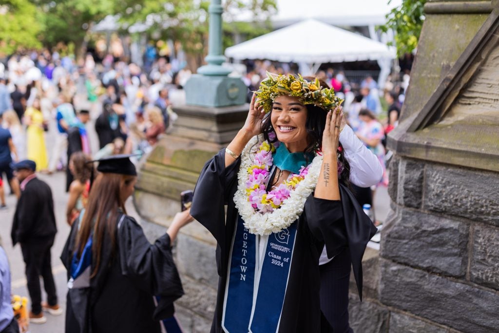 A Georgetown graduate in a cap and gown, wearing a headpiece made of flowers