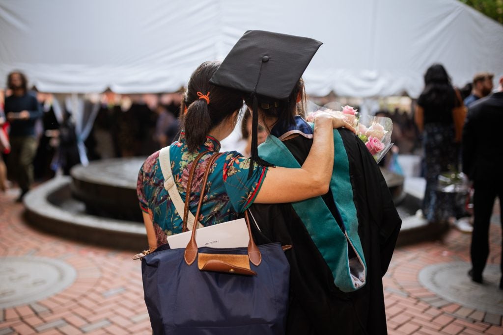 A Georgetown graduate in a cap and gown and a family member pose for a photo. Their backs are to the camera.