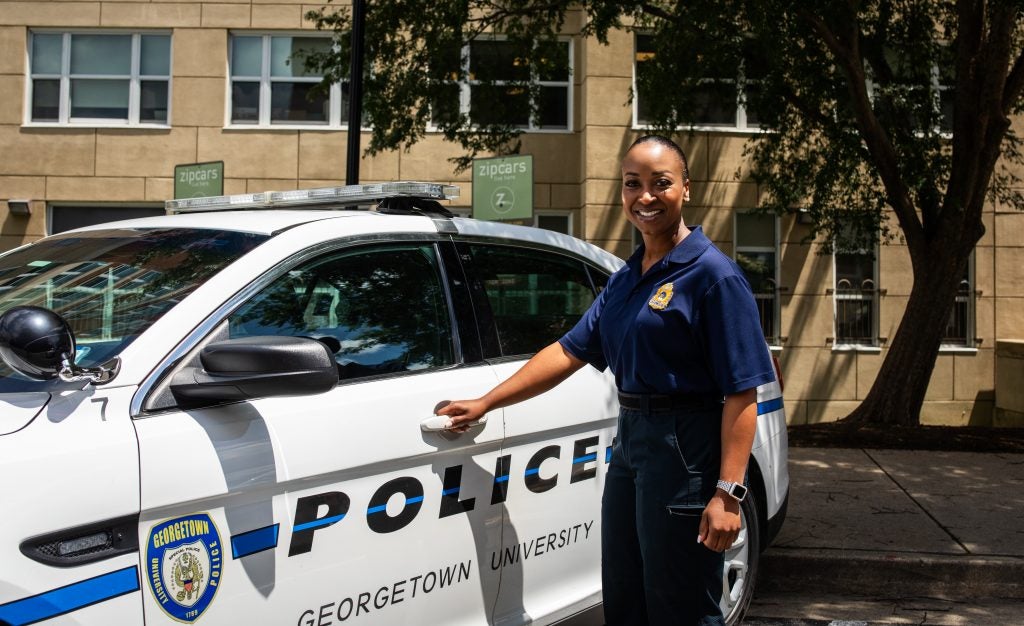 A Black female police officer opens the door of her police car.