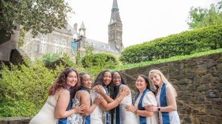 A group of six GU graduates posing for grad photos on the Lauinger Steps on an overcast day