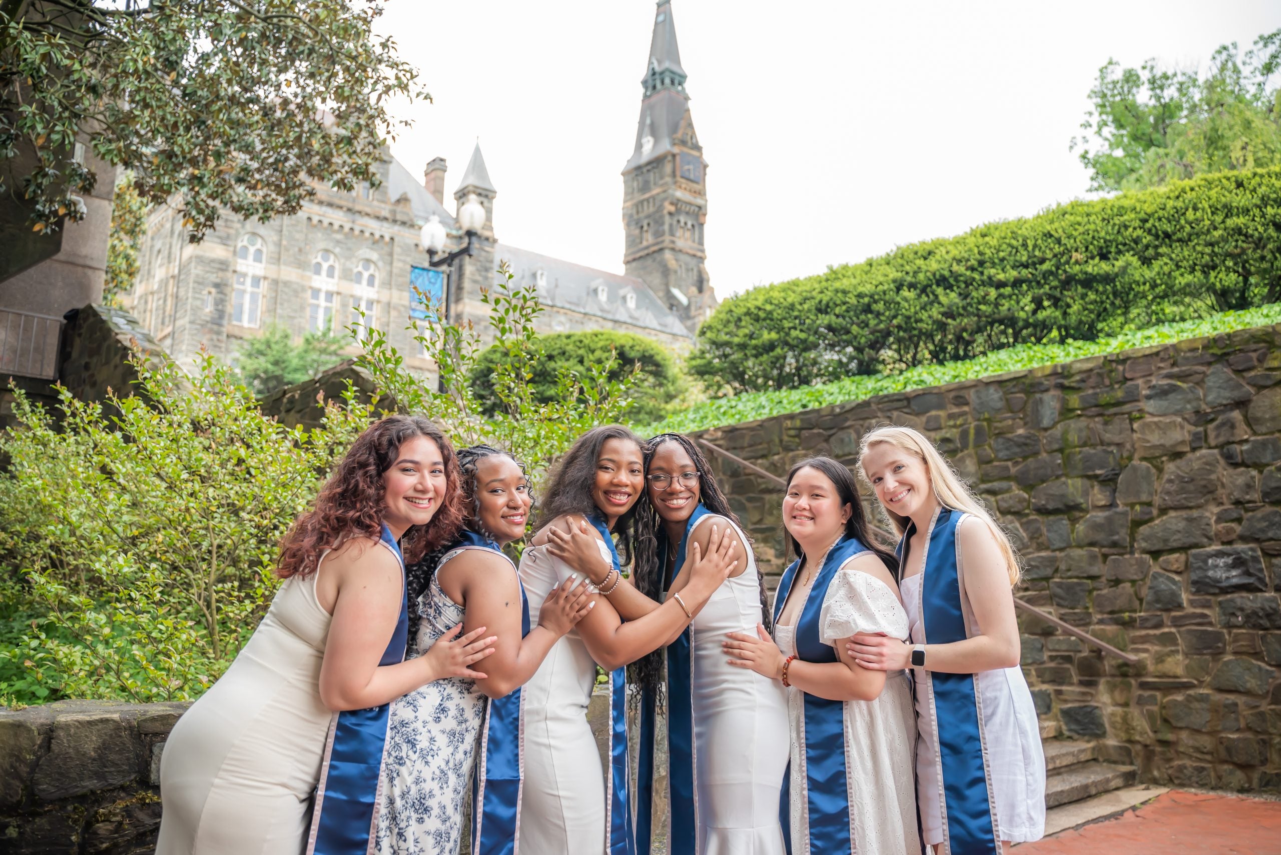 A group of six GU graduates posing for grad photos on the Lauinger Steps on an overcast day