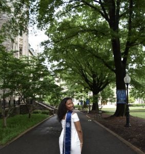 Christine Mauvais walking near Copley Hall while looking back with a white dress and a graduation stole.
