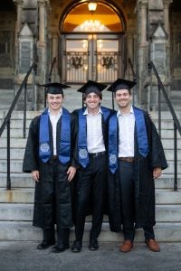 Fleisher with two friends all in  graduation robes in front of Healy Hall steps