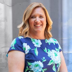 A woman in a blue floral shirt smiles.