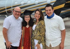 A high school graduate stands with her family.