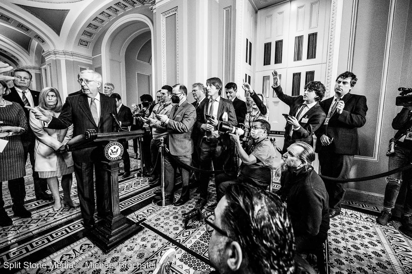Senator Mitch McConnel answers questions from many reporters during a press conference in a black and white photograph.