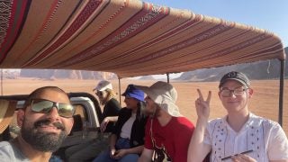 Five people in the back of a truck driving through a desert