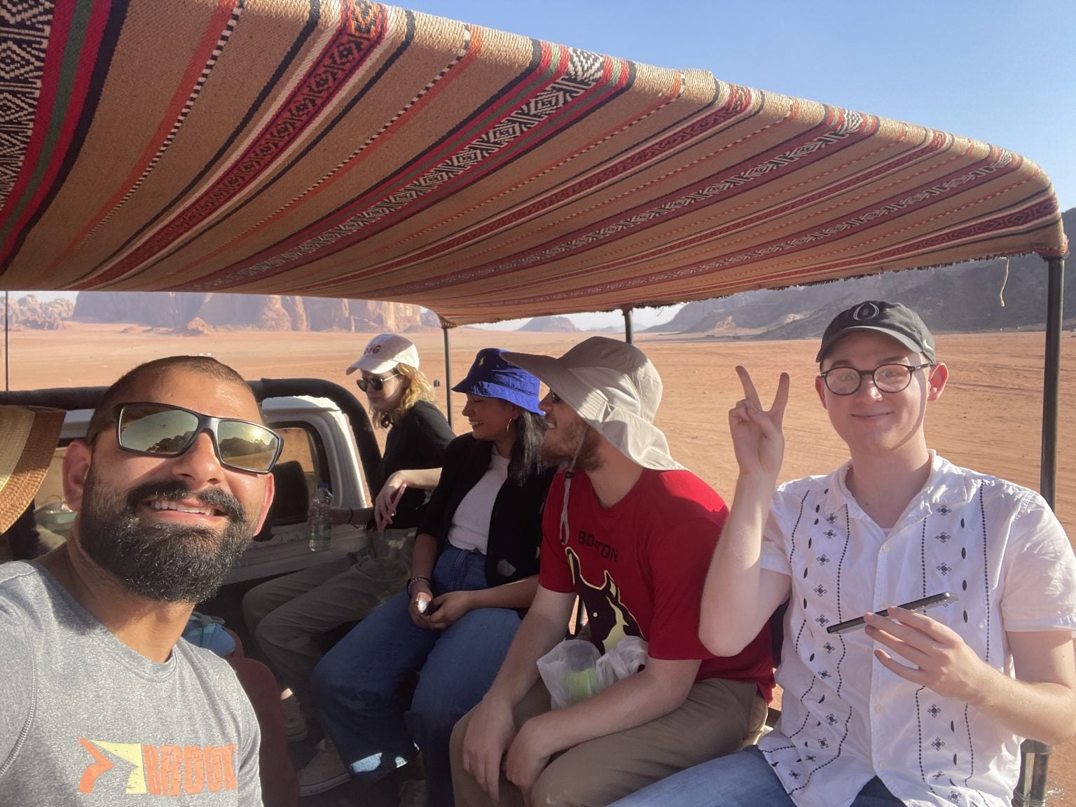 Five people in the back of a truck driving through a desert