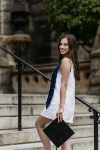 Ava Culoso graduation photo on the steps of Healy Hall holding a grad cap while in a white dress and a blue stole
