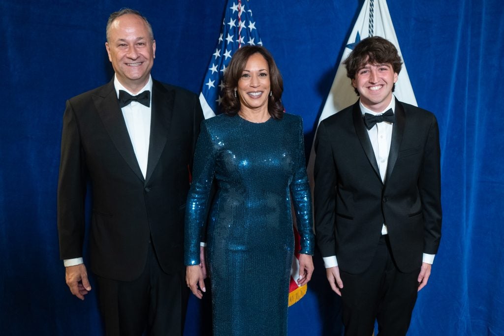 Gabe Fleisher standing with Doug Emhoff and Kamala Harris all wearing formal attire in front of an American flag.