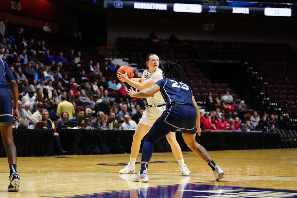 Graceann Bennett holds a basketball in front of a defensive player during a basketball game.