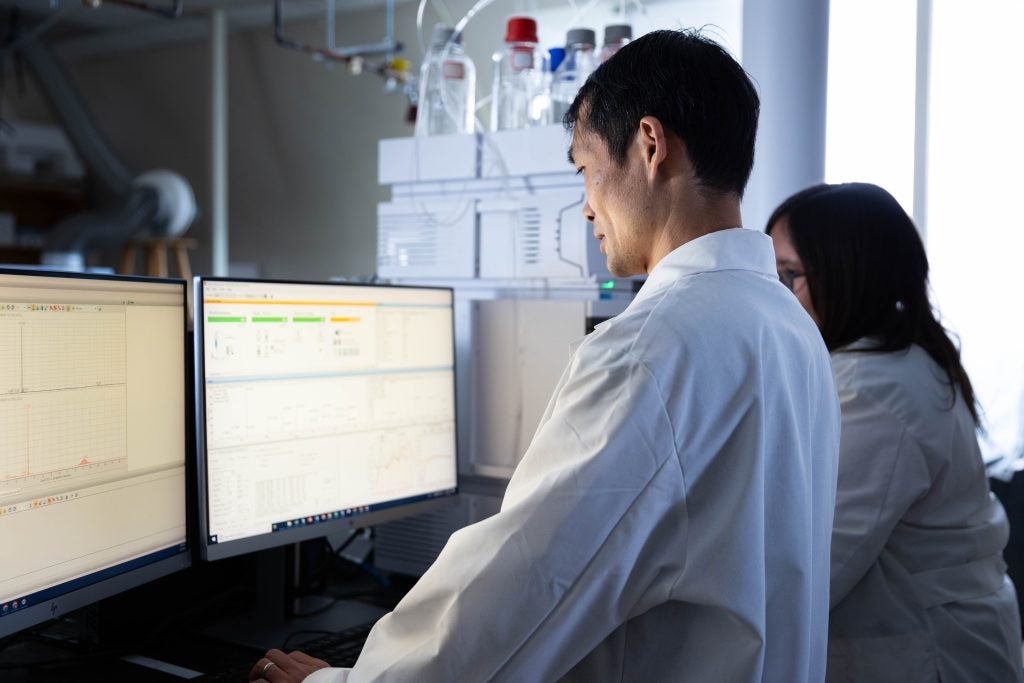 A man in a white lab coat looks at a compute in a laboratory.