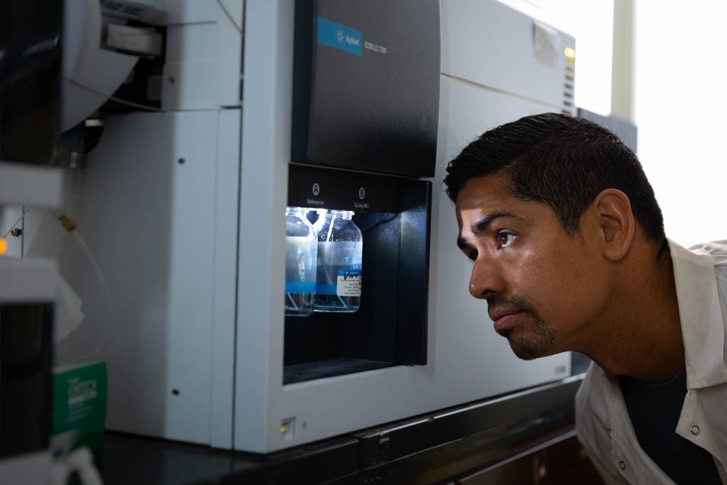 A man peers into an instrument that measures chemicals in water in a lab.