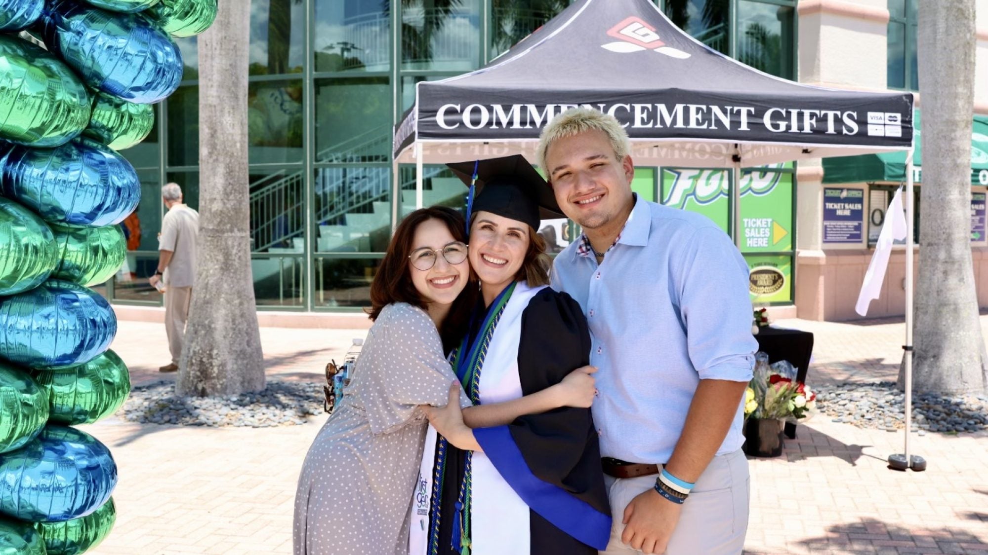 A mother graduates from college and hugs her children in front of balloons. She&#039;s wearing a cap and gown.