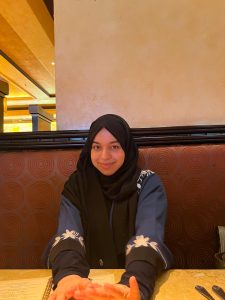 A young woman with a Muslim headdress sitting in a booth