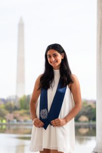 Zehra Mizra graduation photo in a white dress with a blue stole and the Washington Monument in the background