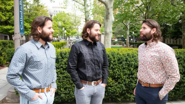 Identical triplets with brown hair and brown beards wear matching &quot;Georgetown Law&quot; T-shirts.