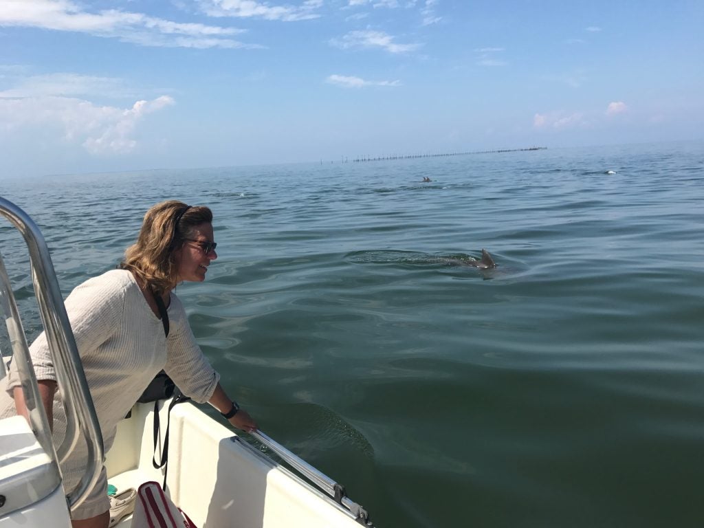 A professor looks over a boat at a dolphin swimming in the water.