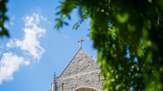 The top of a building with a cross at the top against a blue sky.