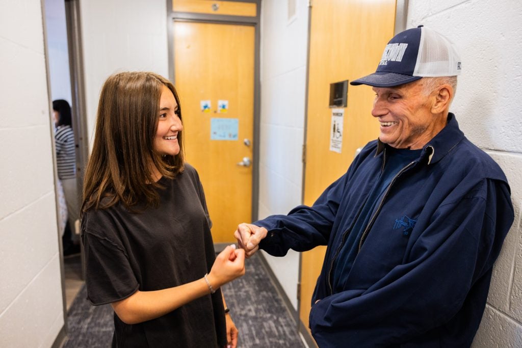 A grandfather in a GU hat fist bumps his granddaughter