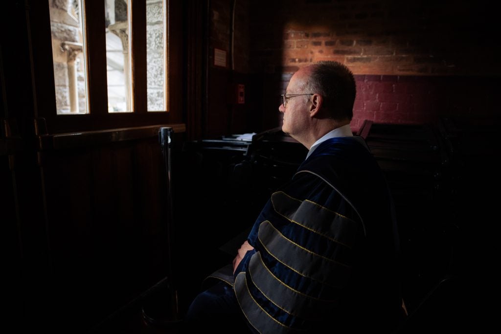 President DeGioia stares out a window in an academic robe