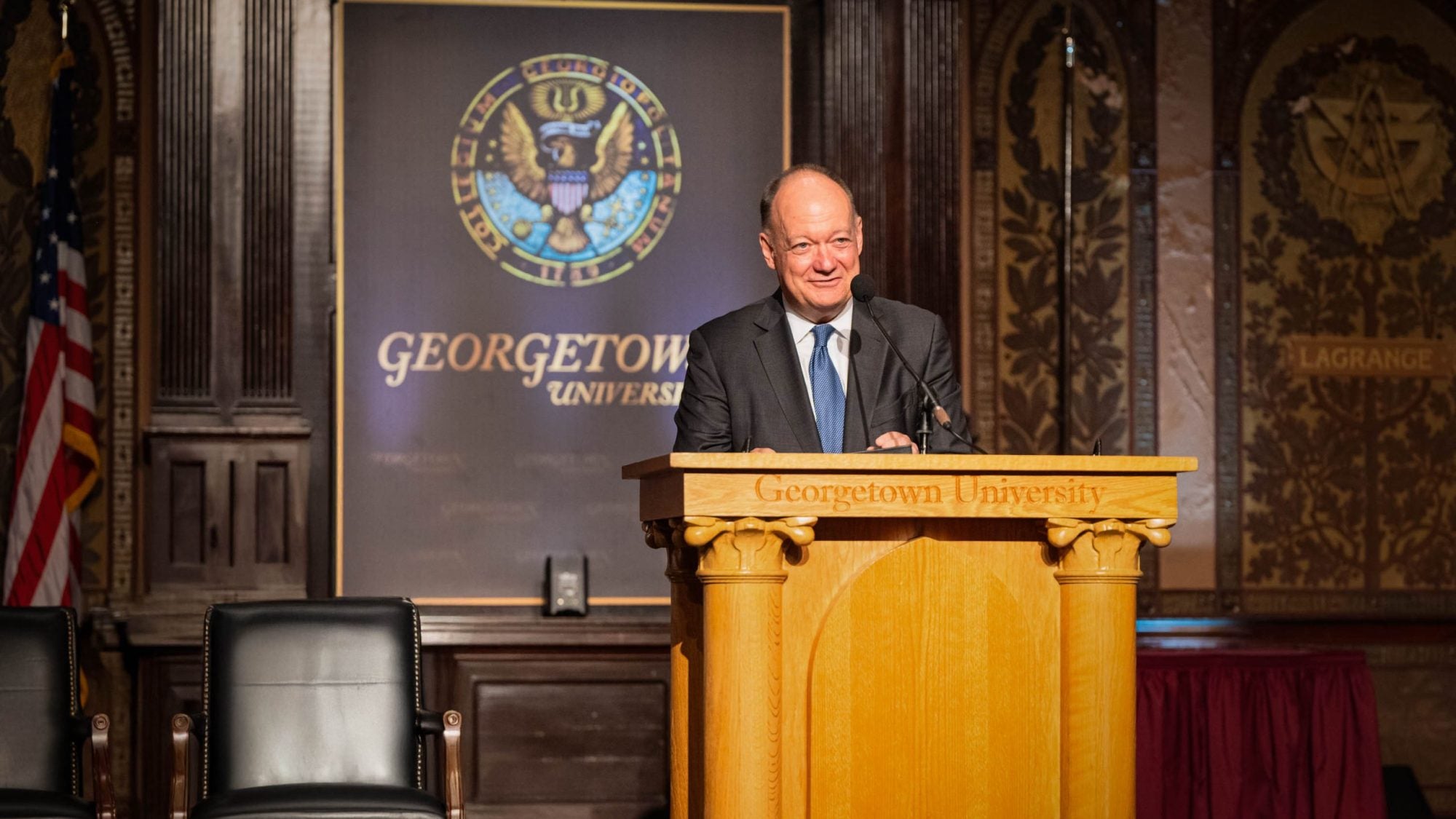 President DeGioia smiles behind a podium in Georgetown&#039;s Gaston Hall.