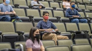 Students sit a few seats apart from each other wearing masks in a lecture hall