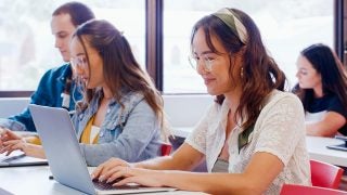 A student smiles while typing on her laptop in a classroom
