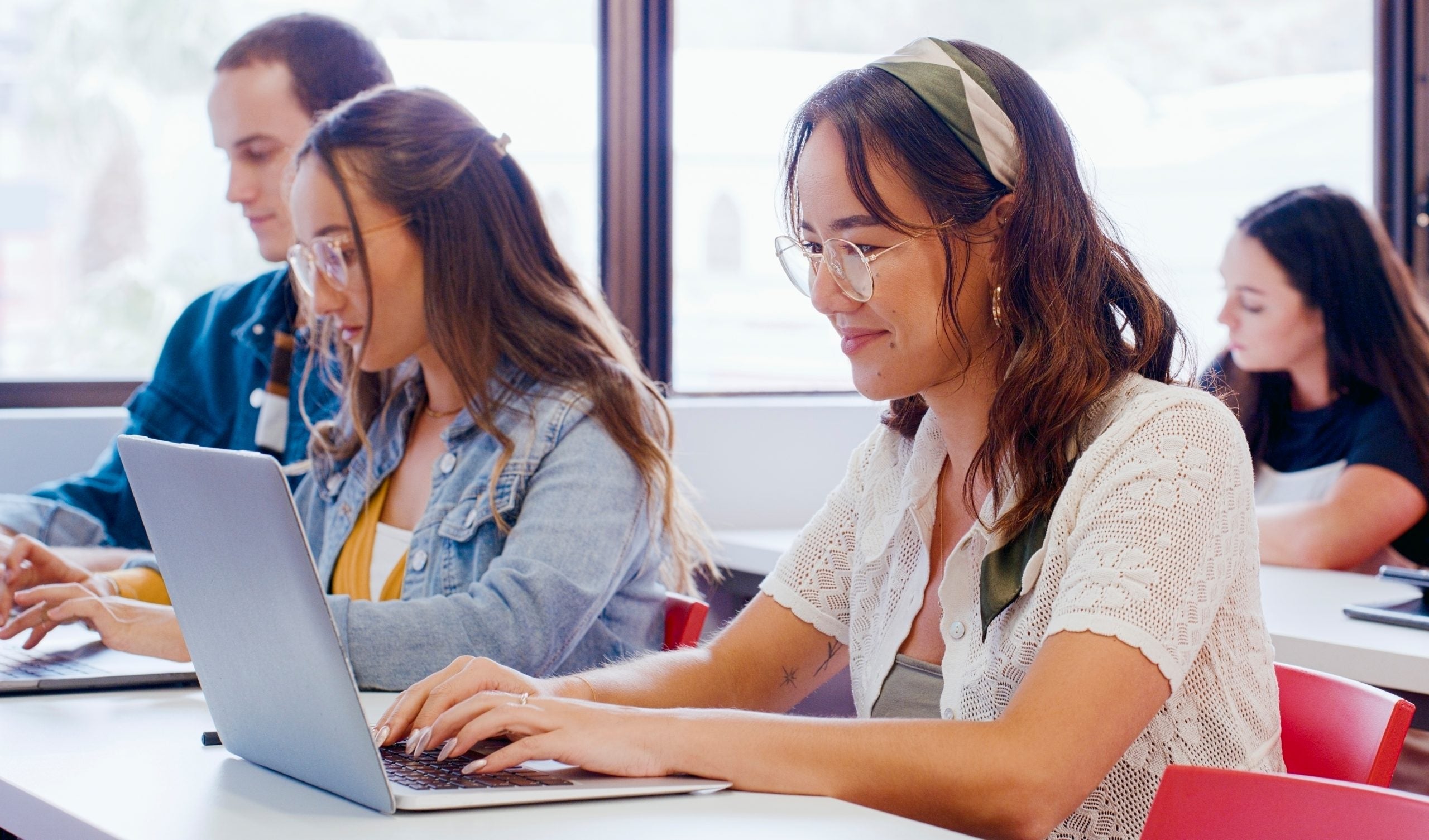 A student smiles while typing on her laptop in a classroom