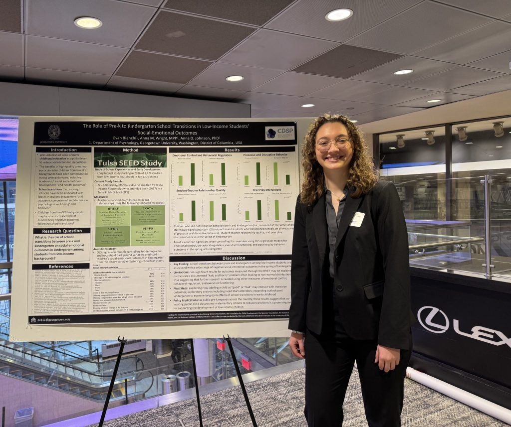 A student stands next to a poster of her research