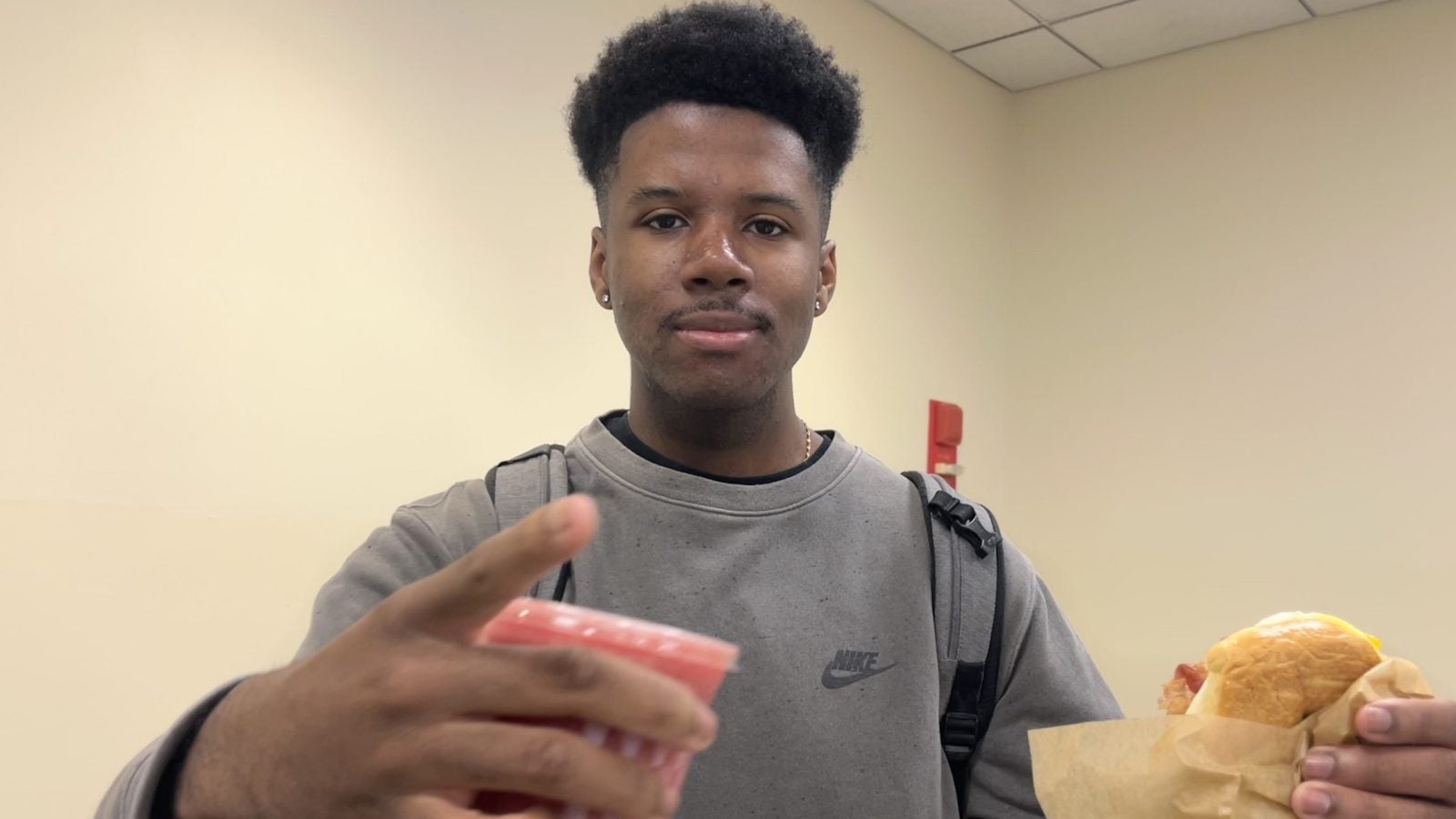 Young Black man holding a sandwich and pink drink