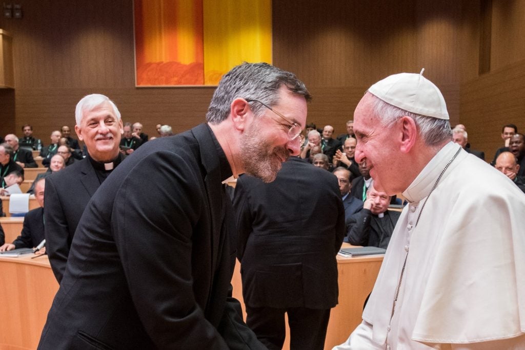 A Jesuit greets Pope Francis. Both smile at each other