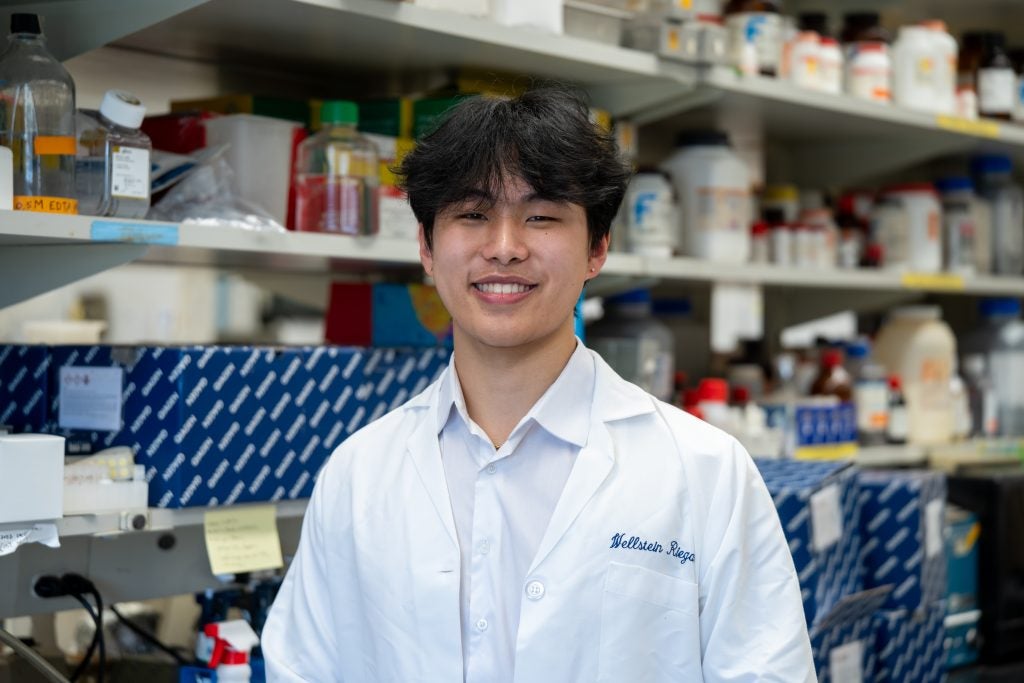 A student in a white lab coat smiles in a laboratory